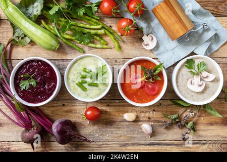 Herbstset mit verschiedenen Gemüsesuppen. Gesunde Ernährung. Vegane heiße Sahnesuppen (Tomaten, Pilze, Rüben, grüne Bohnen) auf rustikalem Holztisch. Ansicht fr Stockfoto