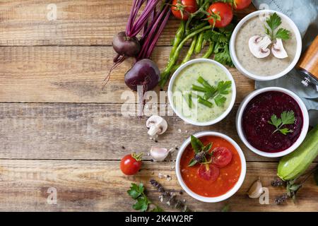 Herbstset mit verschiedenen Gemüsesuppen. Gesunde Ernährung. Vegane heiße Sahnesuppen (Tomaten, Pilze, Rüben, grüne Bohnen) auf rustikalem Holztisch. Ansicht fr Stockfoto