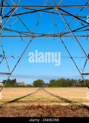 Ich liebe Strommasten; ihre abstrakten, vergilbten Formen finde ich unendlich faszinierend. Hier sehen wir Schatten, die von einem großen Pylon in einem Feld im ländlichen Ra geworfen werden Stockfoto