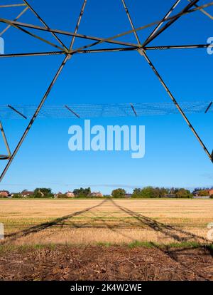 Ich liebe Strommasten; ihre abstrakten, vergilbten Formen finde ich unendlich faszinierend. Hier sehen wir Schatten, die von einem großen Pylon in einem Feld im ländlichen Ra geworfen werden Stockfoto