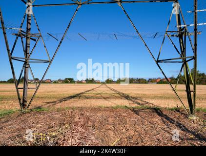 Ich liebe Strommasten; ihre abstrakten, vergilbten Formen finde ich unendlich faszinierend. Hier sehen wir Schatten, die von einem großen Pylon in einem Feld im ländlichen Ra geworfen werden Stockfoto