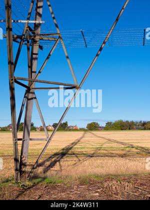 Ich liebe Strommasten; ihre abstrakten, vergilbten Formen finde ich unendlich faszinierend. Hier sehen wir Schatten, die von einem großen Pylon in einem Feld im ländlichen Ra geworfen werden Stockfoto