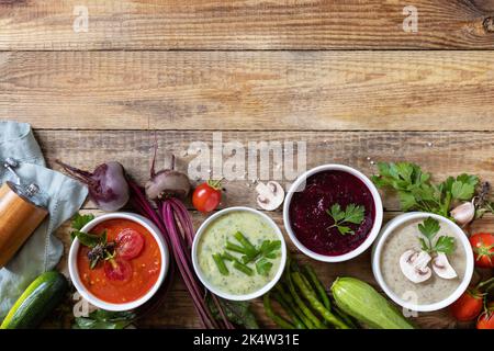 Herbstset mit verschiedenen Gemüsesuppen. Gesunde Ernährung. Vegane heiße Sahnesuppen (Tomaten, Pilze, Rüben, grüne Bohnen) auf rustikalem Holztisch. Ansicht fr Stockfoto