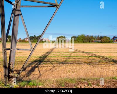 Ich liebe Strommasten; ihre abstrakten, vergilbten Formen finde ich unendlich faszinierend. Hier sehen wir Schatten, die von einem großen Pylon in einem Feld im ländlichen Ra geworfen werden Stockfoto