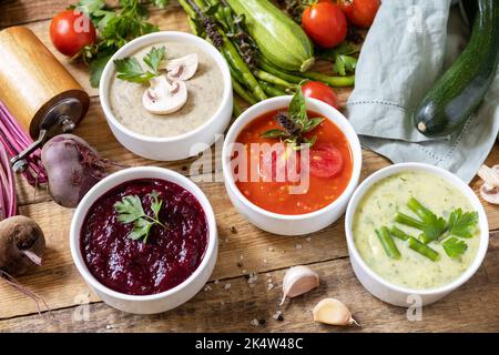 Herbstset mit verschiedenen Gemüsesuppen. Gesunde Ernährung. Vegane heiße Sahnesuppen (Tomaten, Pilze, Rüben, grüne Bohnen) auf rustikalem Holztisch. Stockfoto