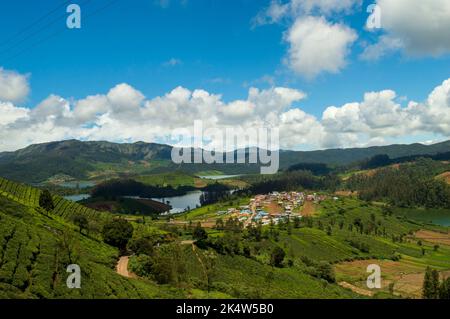 Aufragende Berge, Teeplantagen, Fluss mit sichtbaren kleinen Häusern, blauer und weißer Himmel, Reflexion sichtbar im Wasser, Naturgeschenk jeder Stockfoto