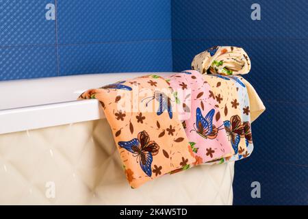 Eine Reihe von bunt gemusterten Handtüchern, die an der Seite einer Badewanne hängen Stockfoto
