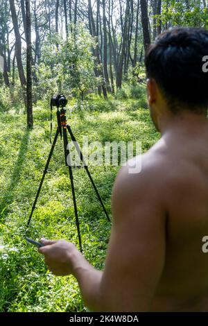 Reifer Sportler mittleren Alters, der in sportlicher Kleidung auf einer Fitnessmatte in Standposition steht, sich online ein Videotutorial zum Training ansieht und vloggt Stockfoto