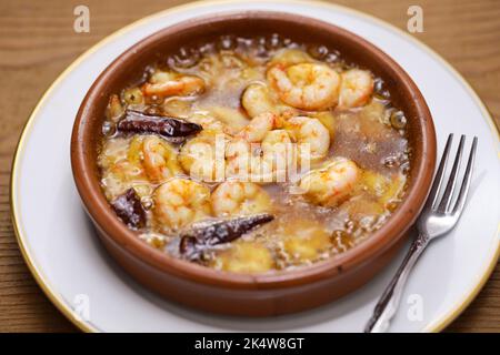 Gambas al Ajillo (Eine spanische Tapas); eine Cazuela, die mit Olivenöl, gehacktem Knoblauch und Chilischoten, Garnelen hinzugefügt, gekocht und heiß serviert wird. Stockfoto