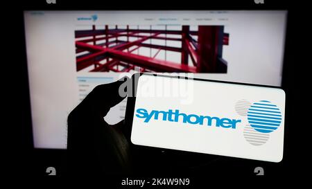 Person, die Mobiltelefon mit dem Logo des britischen Chemieunternehmens Synthomer plc auf dem Bildschirm vor der Business-Webseite hält. Konzentrieren Sie sich auf die Telefonanzeige. Stockfoto