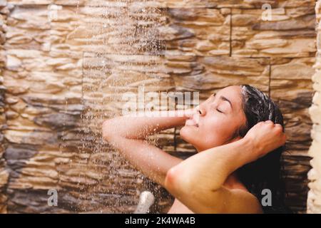 Glückliche Birazialfrau, die duscht und im Badezimmer Haare wäscht Stockfoto