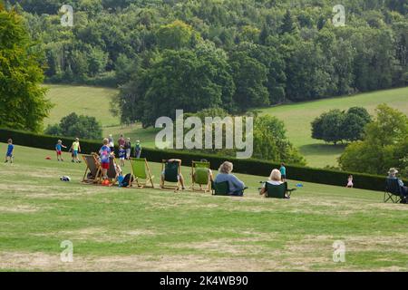 Leute draußen in Liegestühlen auf Rasen des Landhauses in Surrey, England Stockfoto