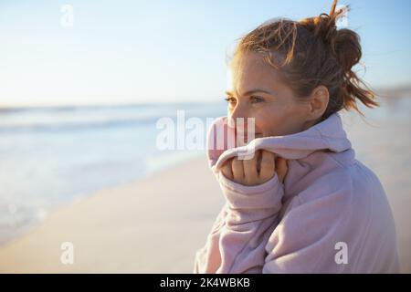 Lächelnde elegante Frau in kuscheligem Pullover am Strand am Abend entspannend. Stockfoto
