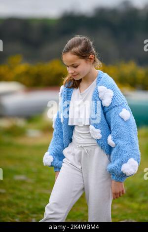 Lächelndes Mädchen in einer Strickjacke, das im Freien läuft Stockfoto