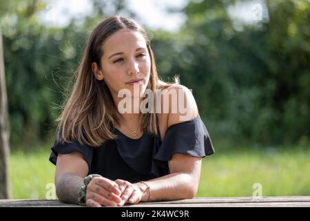 Porträt einer jungen Frau, die sich im Sommer auf einen Holzzaun stützt Stockfoto