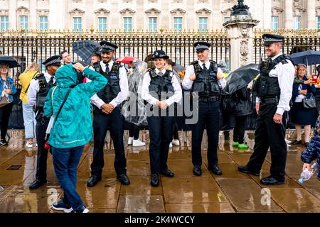 Metropolitan Police Officers stehen vor dem Buckingham Palace in the Rain, London, Großbritannien. Stockfoto