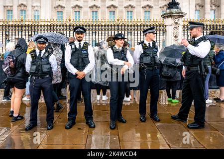 Metropolitan Police Officers stehen vor dem Buckingham Palace in the Rain, London, Großbritannien. Stockfoto
