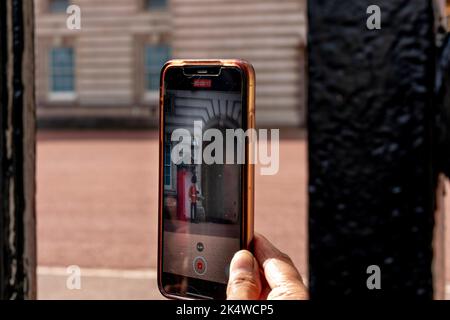 Ein Tourist macht Ein Foto vom Buckingham Palace und Einer Palastwache durch die Tore, Buckingham Palace, London, Großbritannien. Stockfoto