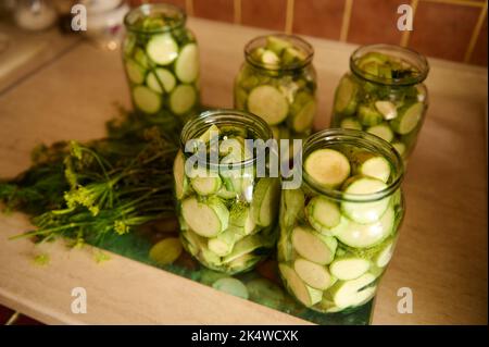 Gläser mit eingelegten Scheiben reifer organischer Zucchini, mariniert in Salzlake, mit frischem Dill, Knoblauchzehen. Lebensmittel Aus Der Konservenindustrie Stockfoto