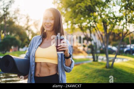 Ruhige sportliche Frau in Sportkleidung mit einer Tasse Kaffee nach dem Training am Morgen im Stadtpark. Fitness-Frau. Schönes junges Mädchen. Aktiv Stockfoto