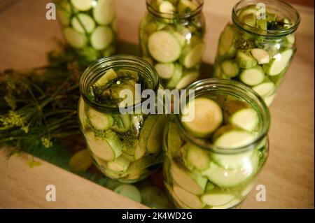Gläser mit eingelegten Scheiben reifer organischer Zucchini, mariniert in Gurke, mit frischem Dill, Knoblauchzehen. Lebensmittel Aus Der Konservenindustrie Stockfoto