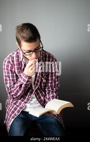 Nahaufnahme eines Mannes mit mittlerem Erwachsenen, der auf einem Stuhl sitzt und ein Buch liest Stockfoto