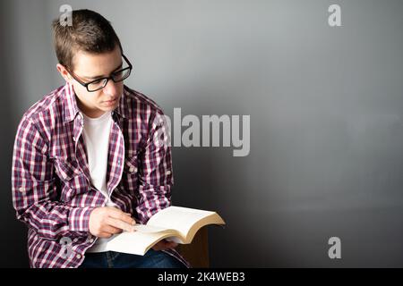 Nahaufnahme eines Mannes mit mittlerem Erwachsenen, der auf einem Stuhl sitzt und ein Buch liest Stockfoto