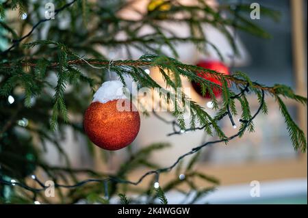 Rote Spielzeugkugel hängt an einem verschneiten Ast, eine rote Kugel an verschneiten Kiefern, Weihnachtsdekoration, Nahaufnahme Stockfoto