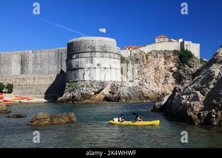 DUBROVNIK, KROATIEN - 18. JULI 2021: Touristen genießen Kajakfahren auf dem Meer vor der mittelalterlichen Stadtmauer der Altstadt von Dubrovnik, die zum UNESCO-Weltkulturerbe gehört. Stockfoto