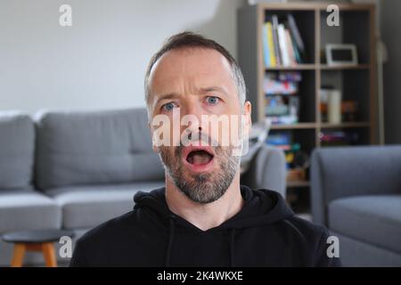 Der Mensch schockiert und ungläubiger Ausdruck. Bärtiger Mann mit lässigem schwarzem Hoodie. Erwachsener kaukasischer Mann im Jahr 30s oder 40s schockiert. Stockfoto