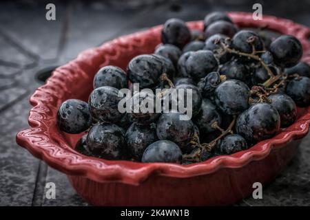 Ein Nahaufnahme von schwarzen Trauben in einer roten Schale Stockfoto
