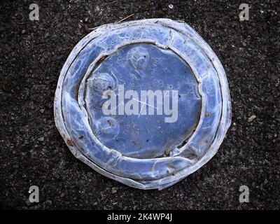 Detail des abgenutzten Plastikbecherdeckels als Müll auf dem Bürgersteig Stockfoto