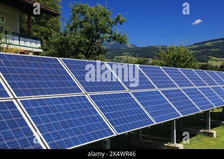 Sonnenkollektoren auf Rahmen im Hof neben einem Privathaus montiert. Photovoltaik-Energieerzeugung bei Salzburg, Österreich. Stockfoto