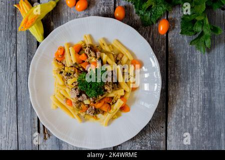 Pasta mit Zucchini, Zucchini-Blumen, gelben Datterini-Tomaten und Wurst auf einem weißen Teller serviert Stockfoto