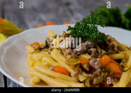 Pasta mit Zucchini, Zucchini-Blumen, gelben Datterini-Tomaten und Wurst auf einem weißen Teller serviert Stockfoto