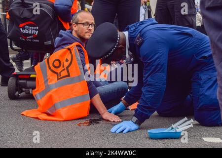 London, England, Großbritannien. 4. Oktober 2022. Ein Polizeibeamter verwendet Lösungsmittel, um den Sekundenkleber auf der Hand eines Protesters von Just Stop Oil aufzulösen, der die Straße auf dem Parliament Square blockiert. Einige Aktivisten klebten ihre Hände an die Straße, und der Protest war Teil einer Reihe von Demonstrationen, die täglich in Westminster stattfanden, wobei die Klimaschutzgruppe ein Ende der fossilen Brennstoffe und einen Wechsel zu erneuerbaren Energien forderte. (Bild: © Vuk Valcic/ZUMA Press Wire) Stockfoto