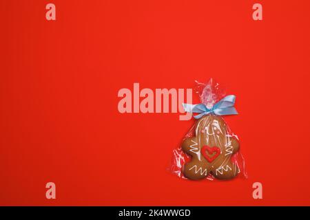 Iced Weihnachten Lebkuchen Mann Zucker Cookie mit rotem Herz eingewickelt In Kunststoff auf rotem Hintergrund Stockfoto