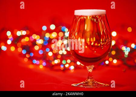 Volles, schniffeltes Glas Lagerbier mit verwackelten weihnachtslichtern auf rotem Hintergrund Stockfoto