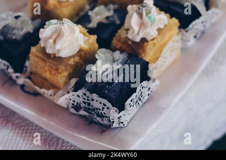 Kleine Scheiben cremiger köstlicher purpurner Yam AKA UBE Cake mit Macapuno-Belag AKA Coconut Sport und Zitronenpudding-Kuchen auf weißem Leinentisch. Stockfoto