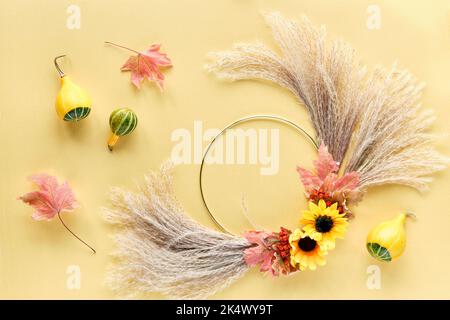 Herbsthintergrund auf gelbem Papier. Getrockneter Blumenkranz und Deko-Kürbisse. Trockene Pampas Gras, Blumen und Herbstblätter auf Metallrahmen. Flach auf Weiß legen Stockfoto