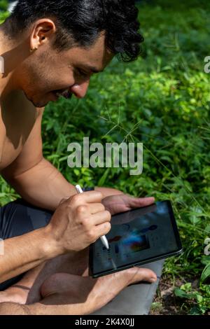 Aktiver schöner männlicher Yogi, der vor oder nach dem Training durch den Wald schlendert. Yoga-Kurs für junge hispanische Sportler mit einer Fitnessmatte Stockfoto