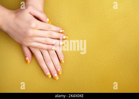 Schöne weibliche Hände mit orangefarbener Maniküre wie Candy Corn. Gepflegte Nägel mit gelbem Gelpolitur. Halloween-Style Stockfoto