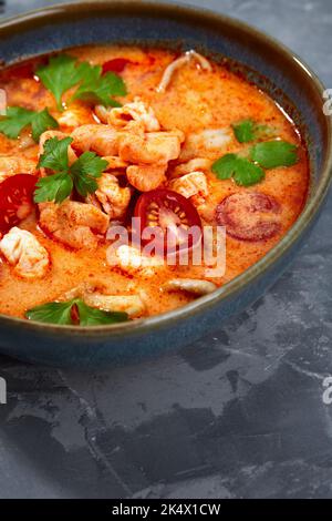 Traditionelle thailändische Küche. Tom Yum würzige Suppe in schwarzer Schüssel auf grauem Hintergrund. Thailändisches Essenskonzept. Draufsicht Stockfoto