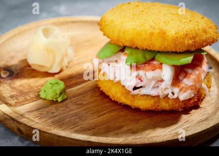 Konzept der panasiatischen Küche. Japanischer Sushi-Burger aus Reisbrot, Krabbenfleisch, Avokado und Wasabi-Sauce. Servieren auf Holzbrett. Platz kopieren Stockfoto