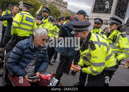 Mit einer behinderten Frau wird von einem Met-Polizeibeamten Climate Change gesprochen, als Protestierende mit Aussterben Rebellion am 3.. Oktober 2022 in London, England, den Verkehr auf dem Trafalgar Square blockieren. Stockfoto