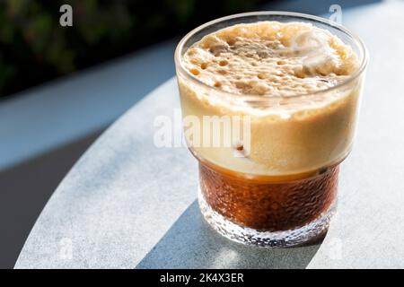 Ein frisch gebrühter Eiskaffee oder ein Getränk, das an einem Tisch vor einem Café serviert wird. Das Getränk hat eine dicke Crema, ein kühles Getränk an einem heißen Tag Stockfoto