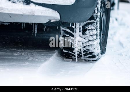 Nahaufnahme eines Winterreifens an einem Fahrzeug, das über eine vereiste oder schneebedeckte Straße fährt. Das detaillierte Profil wurde für verbesserte Traktion und Sicherheit entwickelt Stockfoto