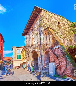 SIRMIONE, ITALIEN - 10. APRIL 2022: Historisches Backsteinhaus mit gewölbtem Pass und Weinreben, die sich entlang der Mauer schlängeln, am 10. April in Sirmione Stockfoto