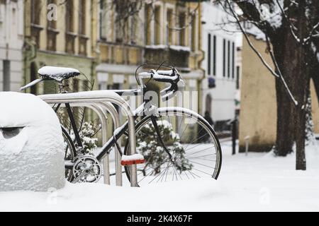 Altes Oldtimer-Fahrrad, mit einer Kette gebunden und vom Schnee bedeckt, der auf der Straße der Altstadt von Vilnius geparkt ist Stockfoto