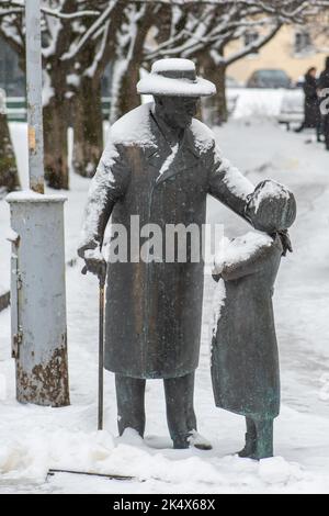 Zemach Shabad Bronzestatue, die sich um ein Mädchen und ihre Kitty, einen Arzt und eine Figur der Vilnius-Gesellschaft aus der ersten Hälfte des 20.. Jahrhunderts mit Schnee kümmert Stockfoto